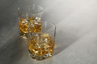 Whiskey with ice cubes in glasses on grey marble table, space for text