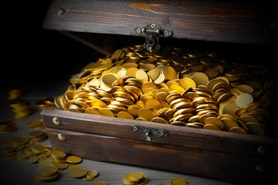 Open treasure chest with gold coins on grey wooden table, closeup 