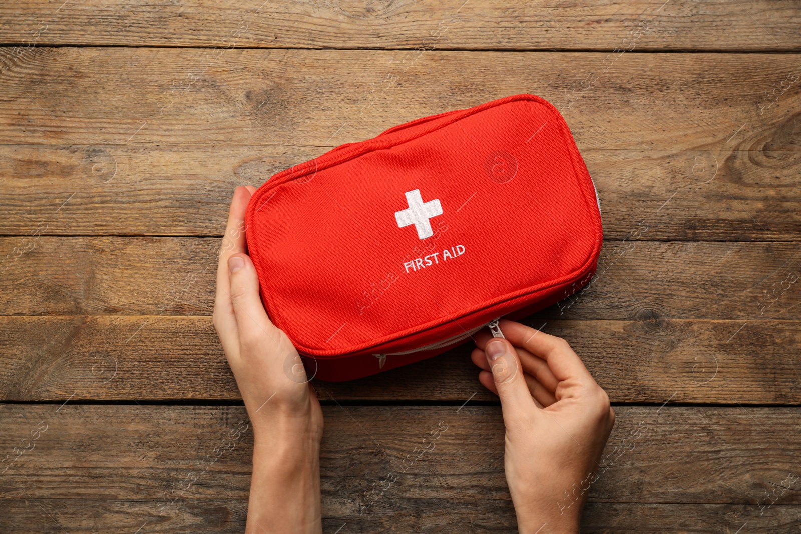 Photo of Woman opening first aid kit bag at wooden table, top view