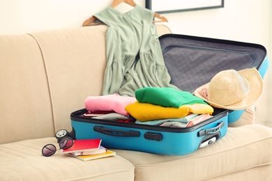 Photo of Travel suitcase with clothes and notebooks on sofa