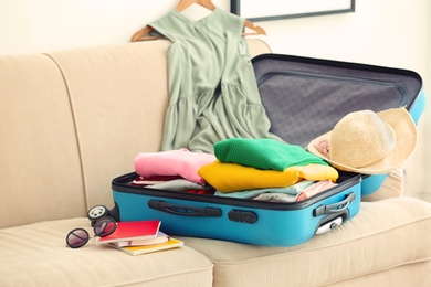 Travel suitcase with clothes and notebooks on sofa