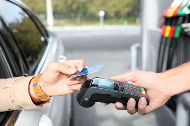 Man sitting in car and paying with credit card at gas station, closeup