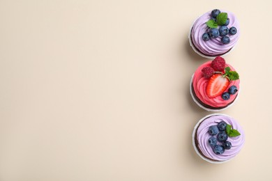 Photo of Different delicious cupcakes with cream and berries on beige background, flat lay. Space for text