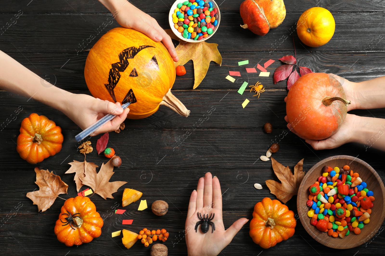 Photo of Women preparing Halloween pumpkin head jack lantern and holiday decorations on wooden table, flat lay composition with space for text