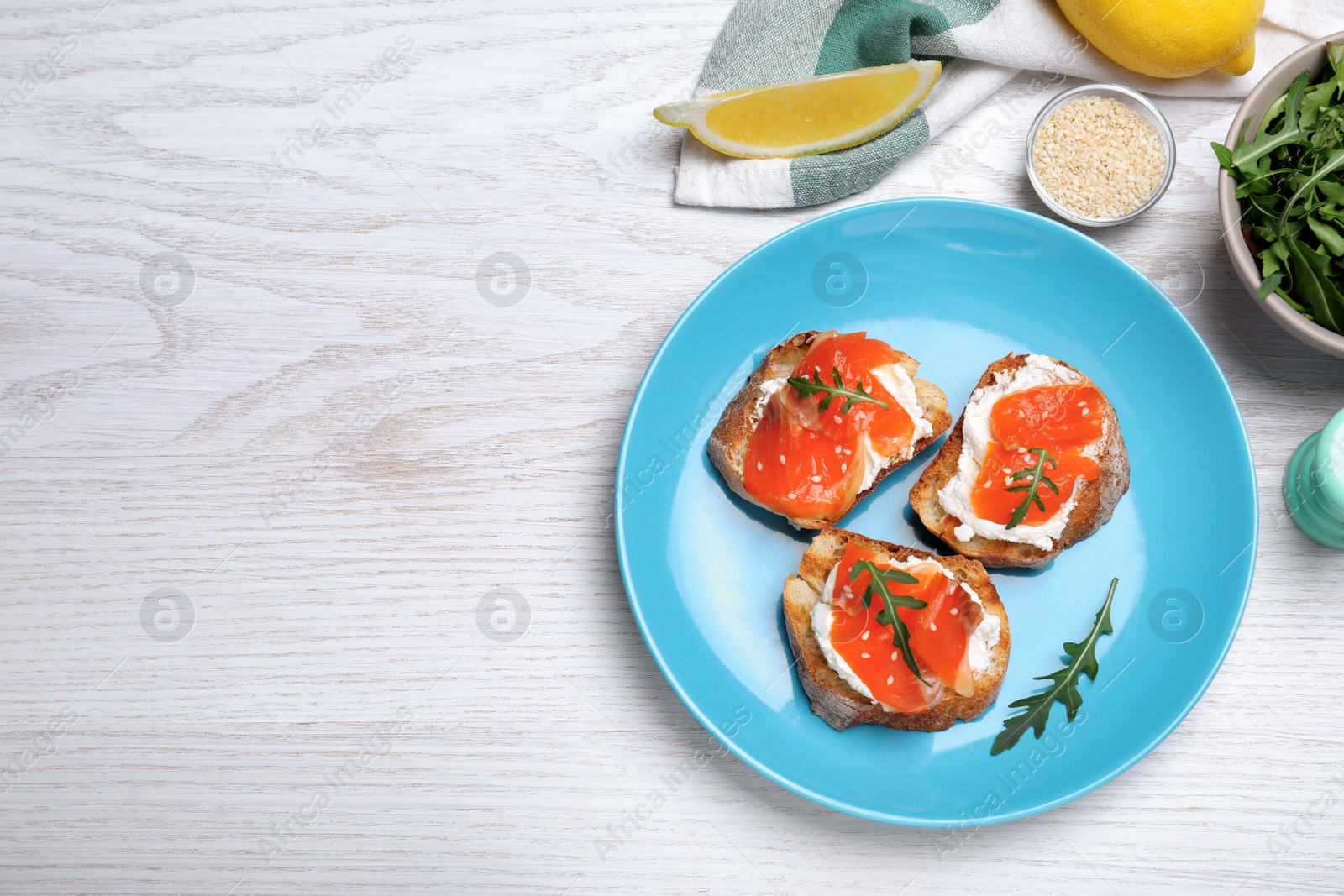 Photo of Delicious sandwiches with cream cheese, salmon and arugula served on white wooden table, flat lay. Space for text