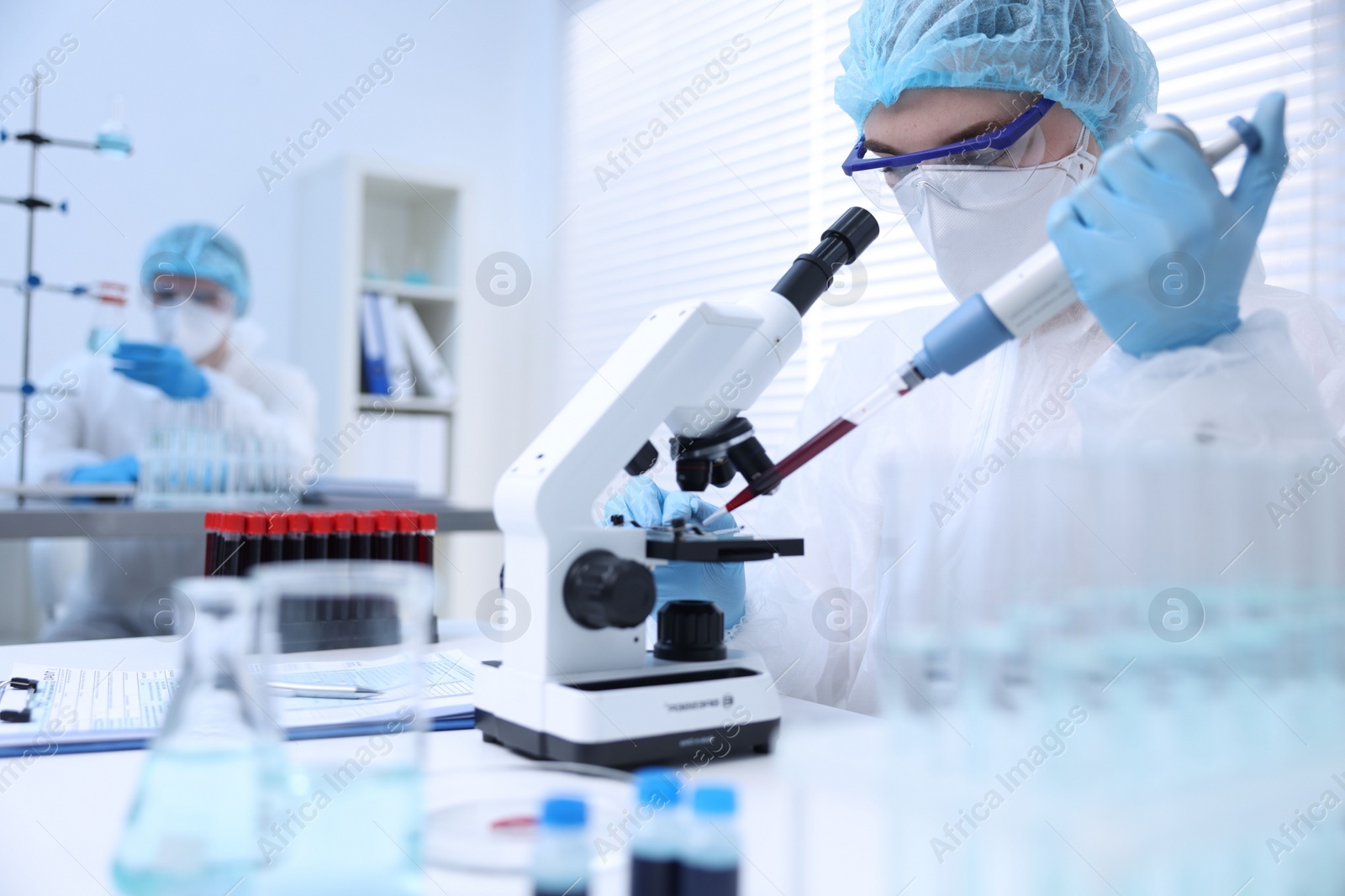 Photo of Scientist dripping sample onto glass slide while working with microscope in laboratory