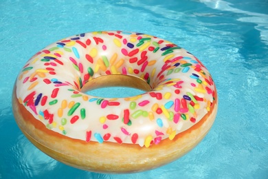 Photo of Bright inflatable doughnut ring floating in swimming pool on sunny day