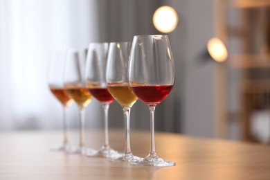 Photo of Different sorts of wine in glasses prepared for tasting on wooden table indoors