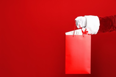 Photo of Santa holding paper bag with gift boxes on red background, closeup. Space for text