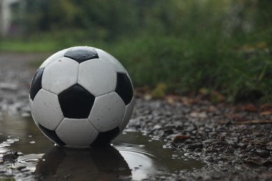 Photo of Leather soccer ball in puddle outdoors, space for text