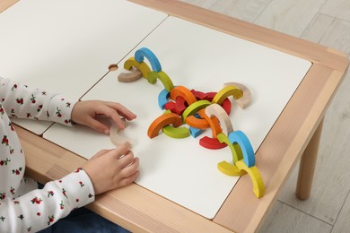 Photo of Motor skills development. Girl playing with colorful wooden arcs at white table indoors, closeup