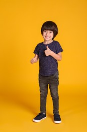 Full length portrait of cute little boy on yellow background