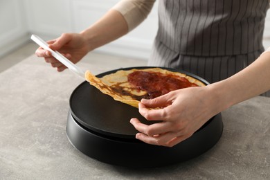 Woman cooking delicious crepe with jam on electric pancake maker in kitchen, closeup