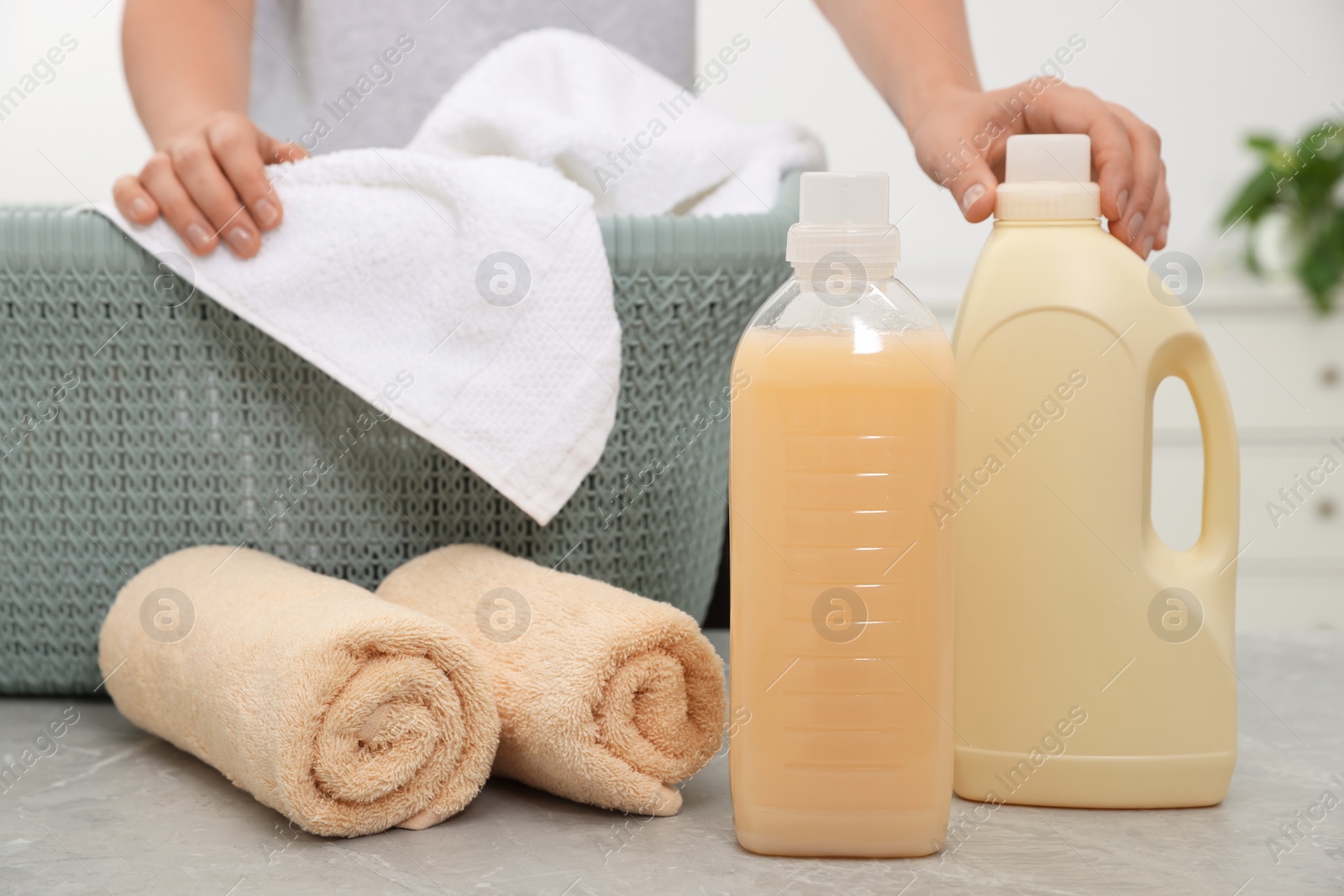 Photo of Woman taking bottle of laundry detergent at light grey table, closeup