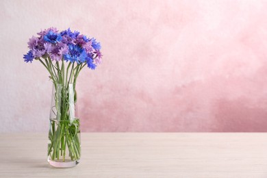 Photo of Bouquet of beautiful cornflowers in glass vase on white wooden table. Space for text