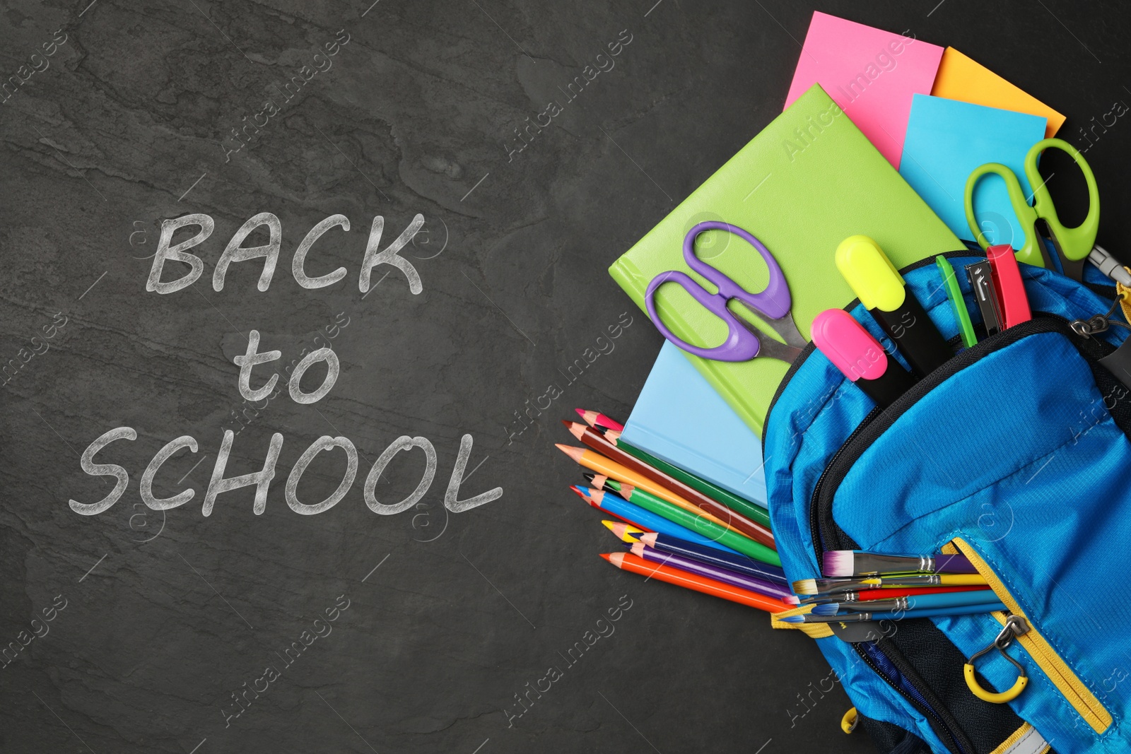 Image of Text Back To School and backpack with different stationery on black chalkboard, top view