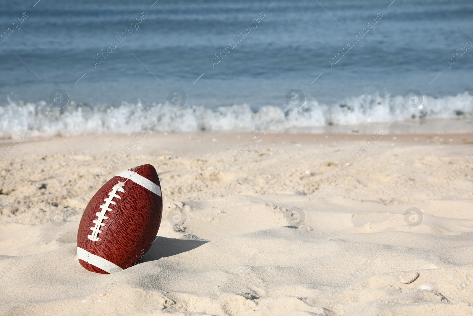 Photo of American football ball on beach. Space for text