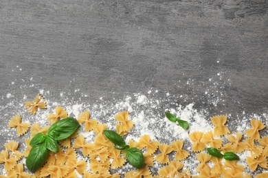 Composition with uncooked farfalle pasta, flour and basil on grey background, top view