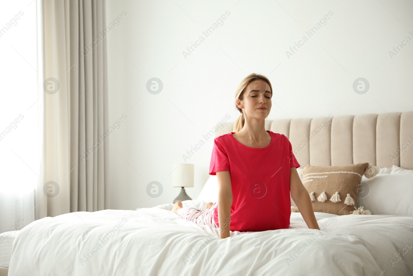 Photo of Young woman doing gymnastics on bed at home. Morning fitness