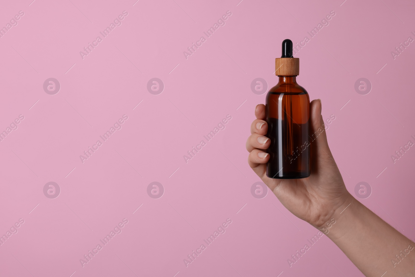 Photo of Woman holding bottle of cosmetic product on pink background, closeup. Space for text