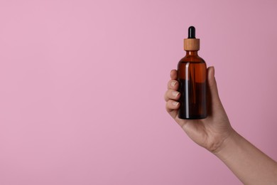 Photo of Woman holding bottle of cosmetic product on pink background, closeup. Space for text