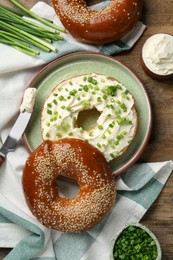 Delicious bagel with cream cheese and green onion on wooden table, flat lay