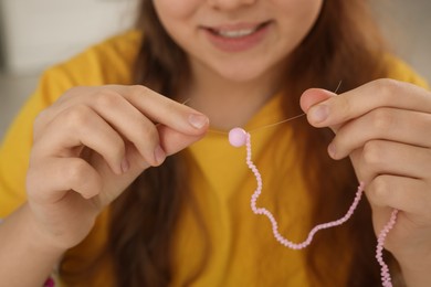 Photo of Happy girl making pink beaded jewelry, closeup