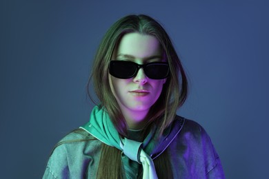 Portrait of beautiful young woman with sunglasses on color background with neon lights