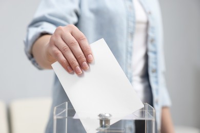 Photo of Woman putting her vote into ballot box on blurred background, closeup