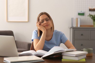 Young tired woman studying at wooden table in room