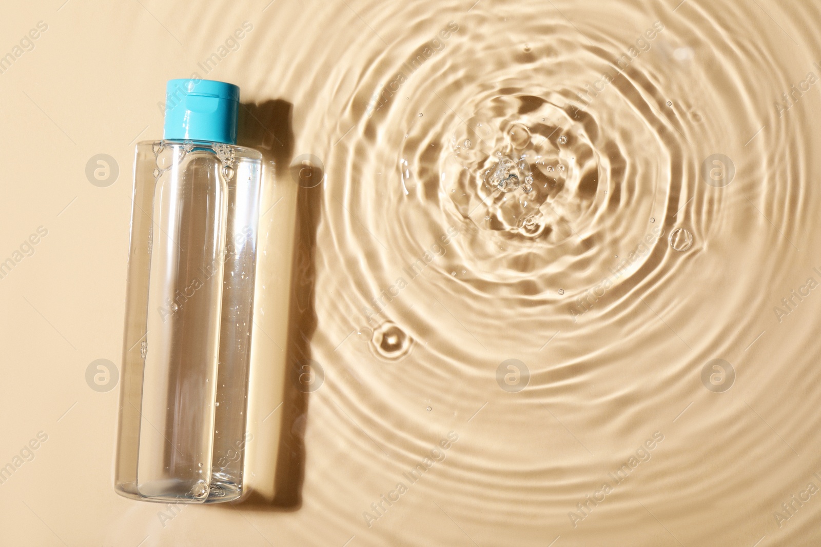 Photo of Wet bottle of micellar water on beige background, top view. Space for text