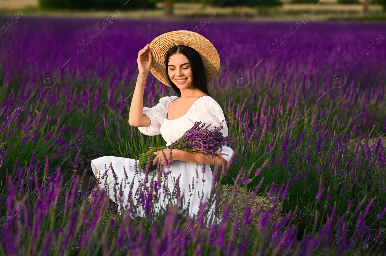 Photo of Beautiful young woman with bouquet sitting in lavender field