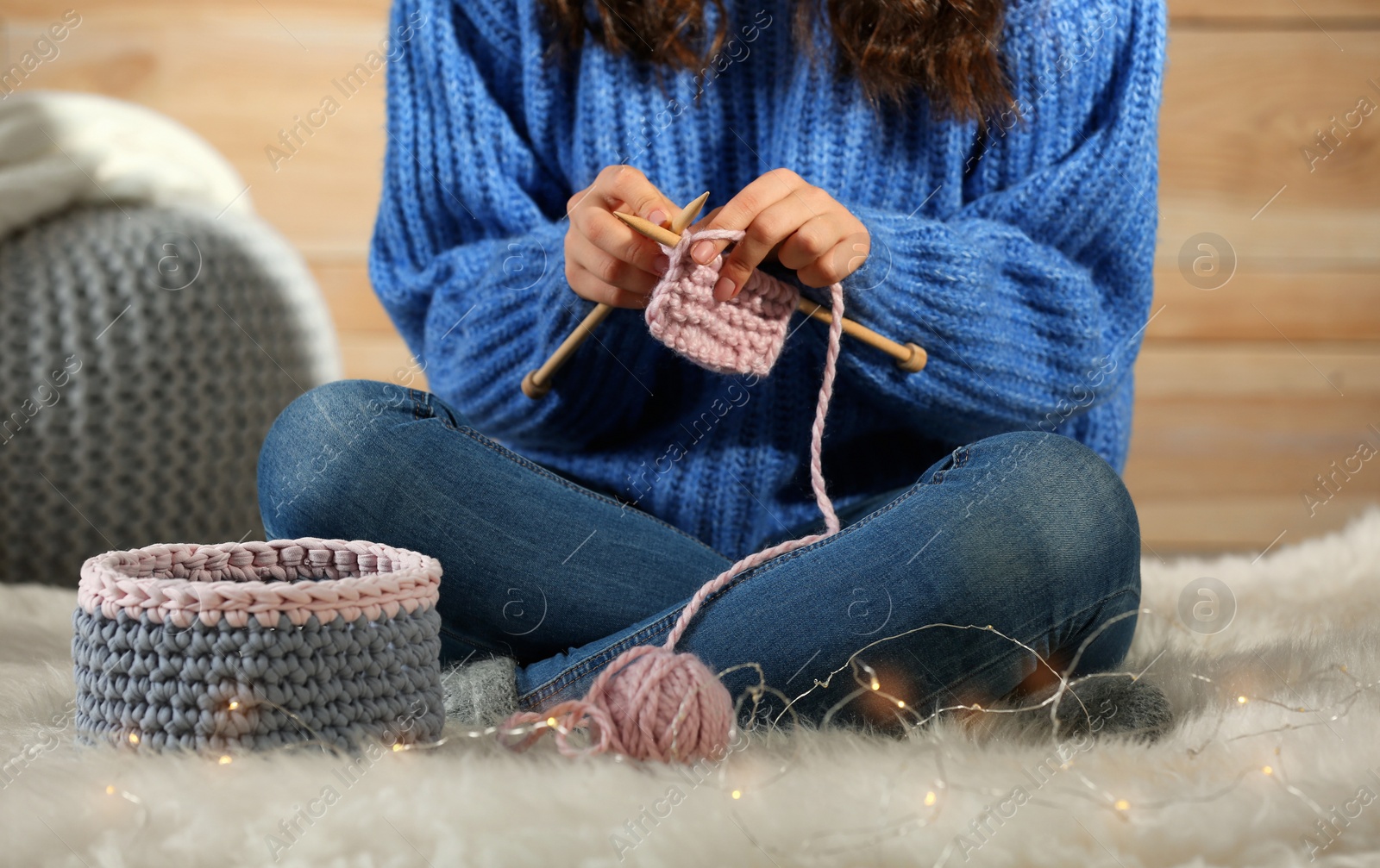 Photo of Woman in warm sweater knitting on fluffy rug at home