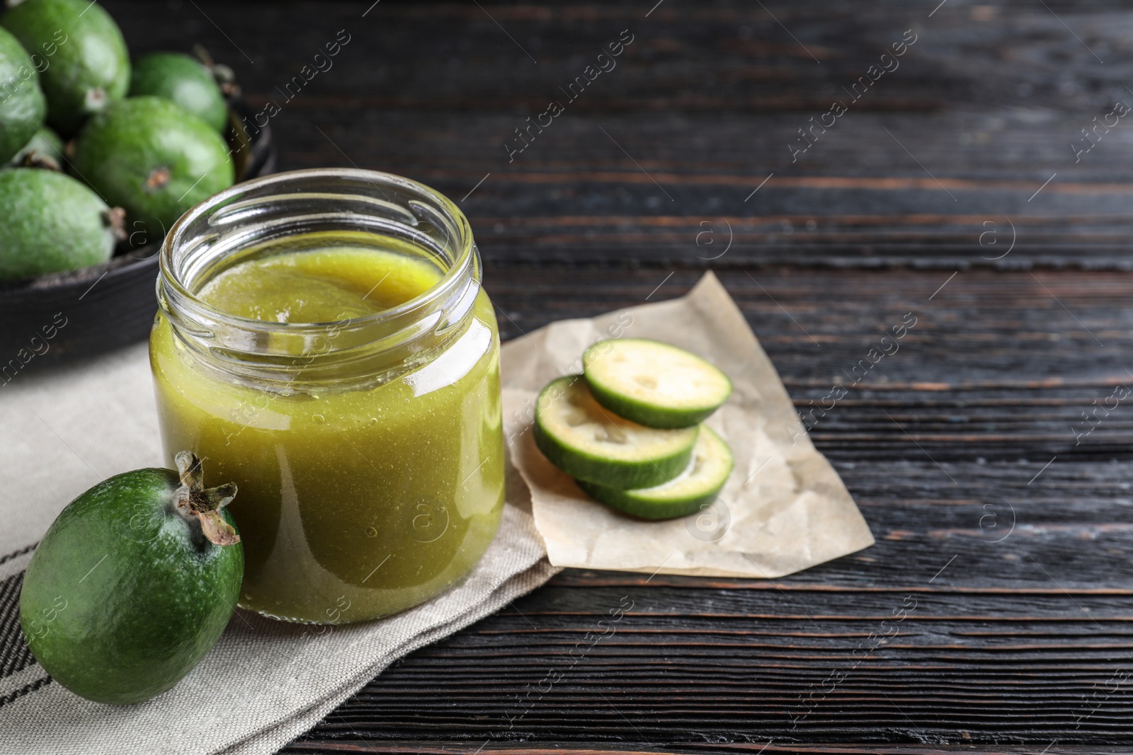 Photo of Feijoa jam and fresh fruit on black wooden table. Space for text
