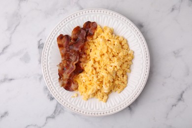 Delicious scrambled eggs with bacon in plate on white marble table, top view