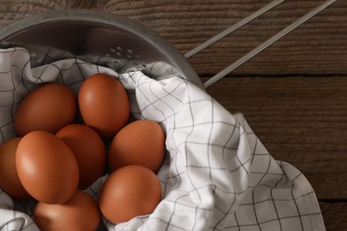 Photo of Chicken eggs in colander with napkin on wooden table, top view. Space for text