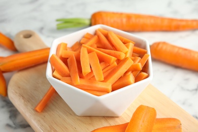 Bowl with cut ripe carrot on wooden board