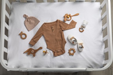 Flat lay composition with cute baby clothes and accessories on white bedsheet in crib