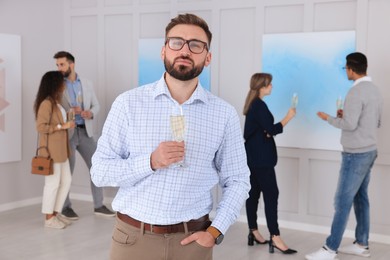 Photo of Young man with glass of champagne at exhibition in art gallery