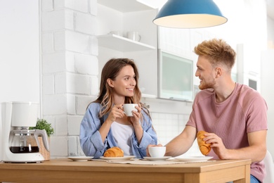 Photo of Happy young couple having breakfast at table in kitchen