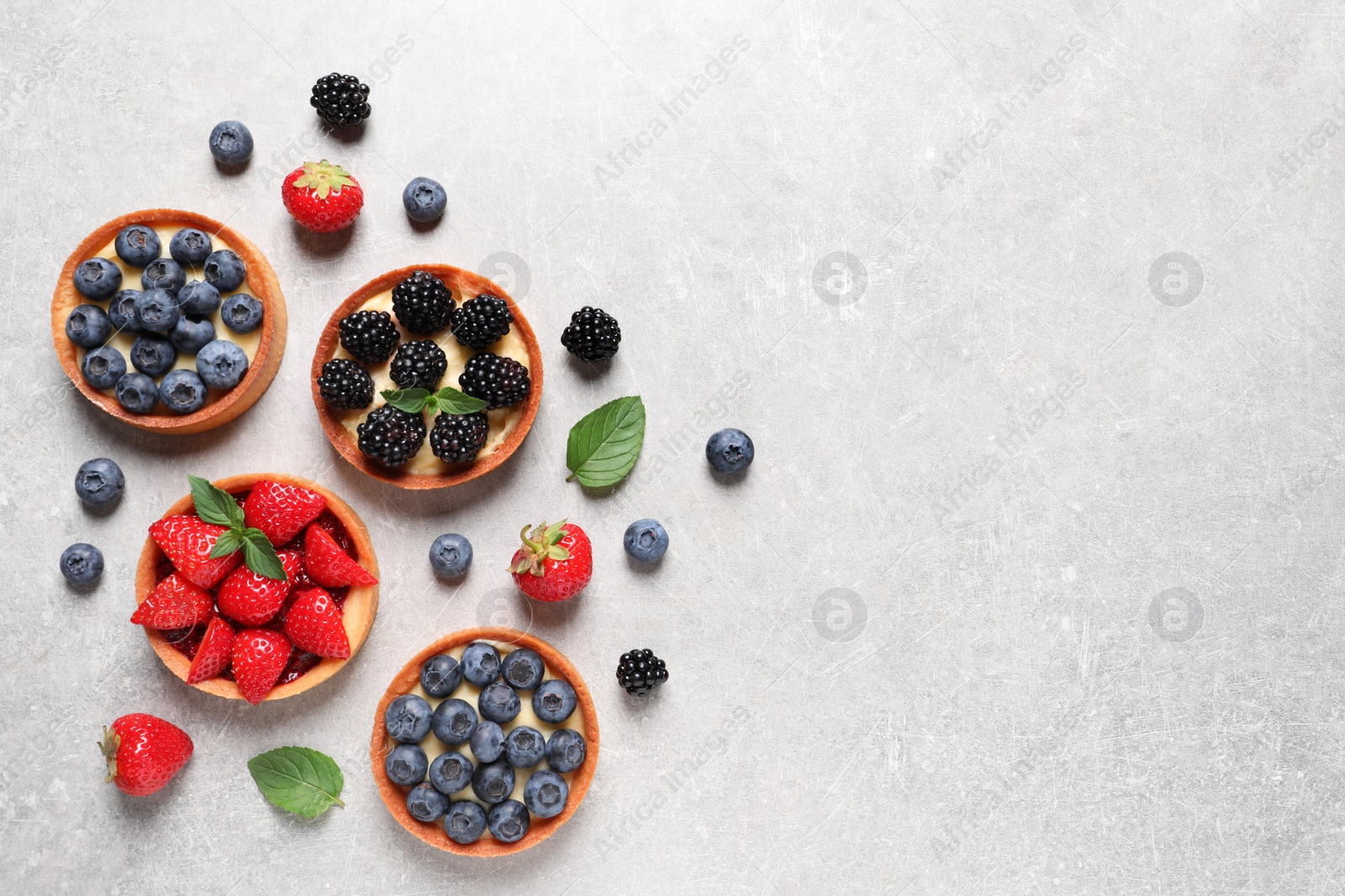 Photo of Tartlets with different fresh berries on light grey table, flat lay and space for text. Delicious dessert