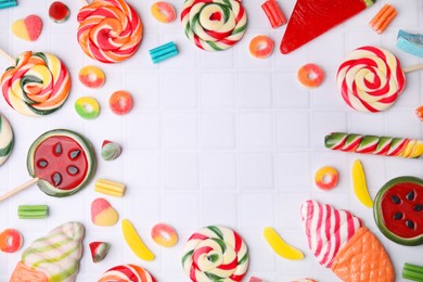 Photo of Frame of tasty colorful jelly candies and lollipops on white tiled table, flat lay. Space for text