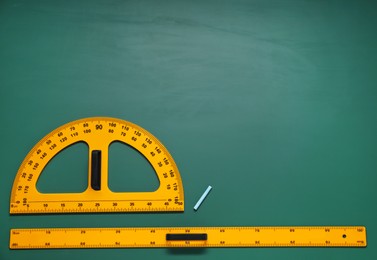 Photo of Protractor, ruler and chalk on green chalkboard, flat lay. Space for text