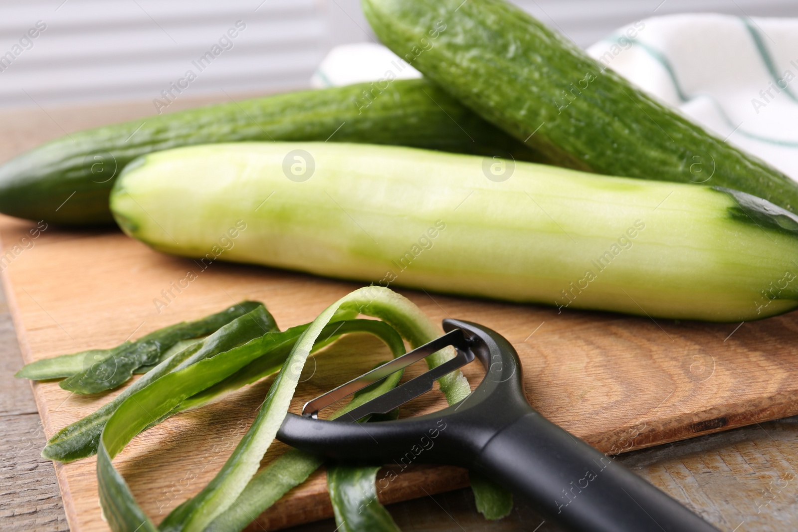 Photo of Fresh cucumbers, peels and peeler on wooden table, closeup