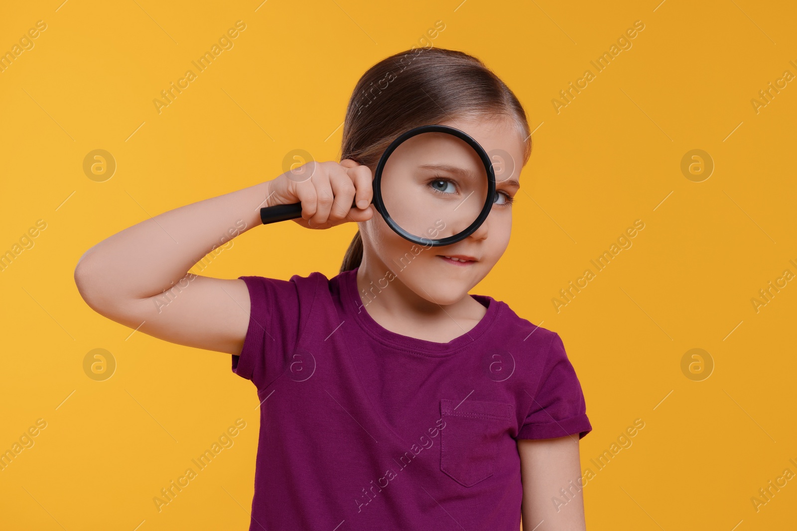 Photo of Cute little girl looking through magnifier on orange background