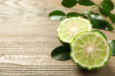 Halves of ripe bergamot fruit and green leaves on wooden table, closeup. Space for text