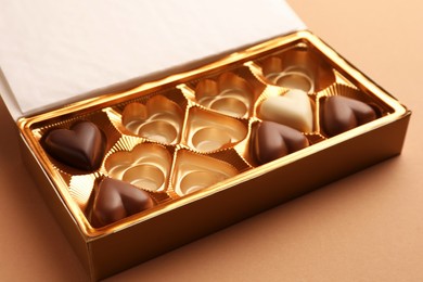 Photo of Partially empty box of chocolate candies on light brown background, closeup