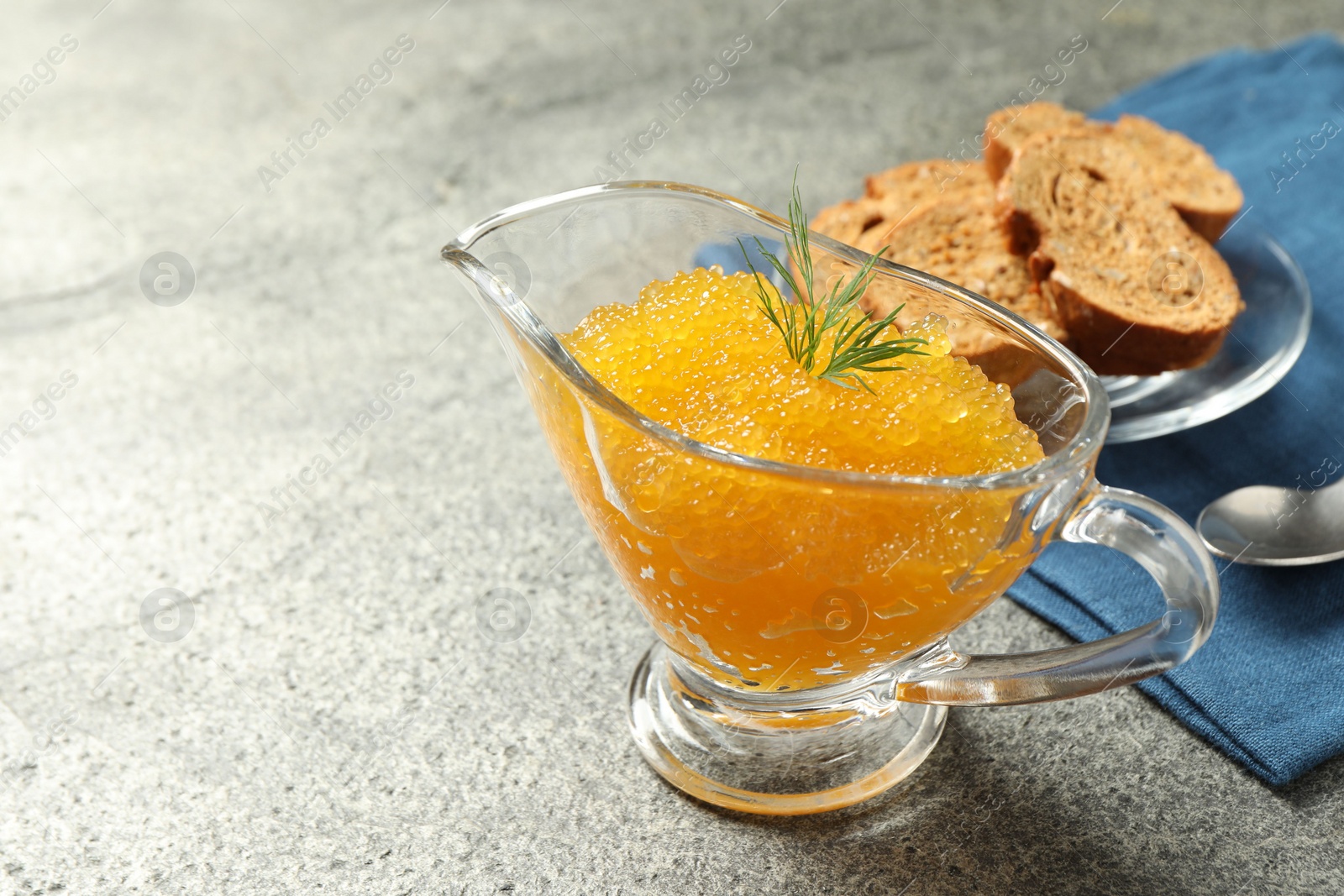 Photo of Fresh pike caviar in gravy boat, bread and spoon on grey table, closeup. Space for text