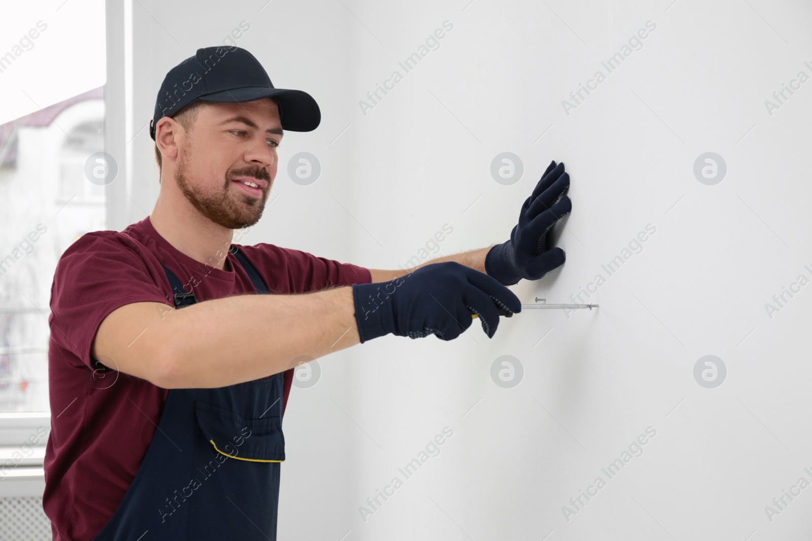 Photo of Handyman in uniform working with screwdriver indoors. Professional construction tools