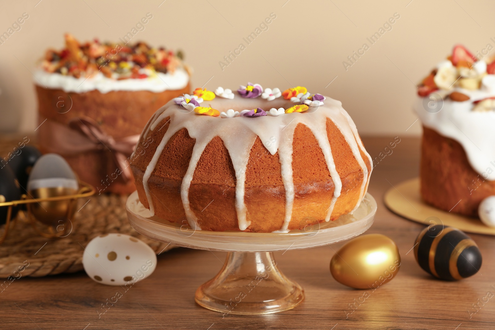 Photo of Delicious Easter cakes decorated with sprinkles near painted eggs on wooden table